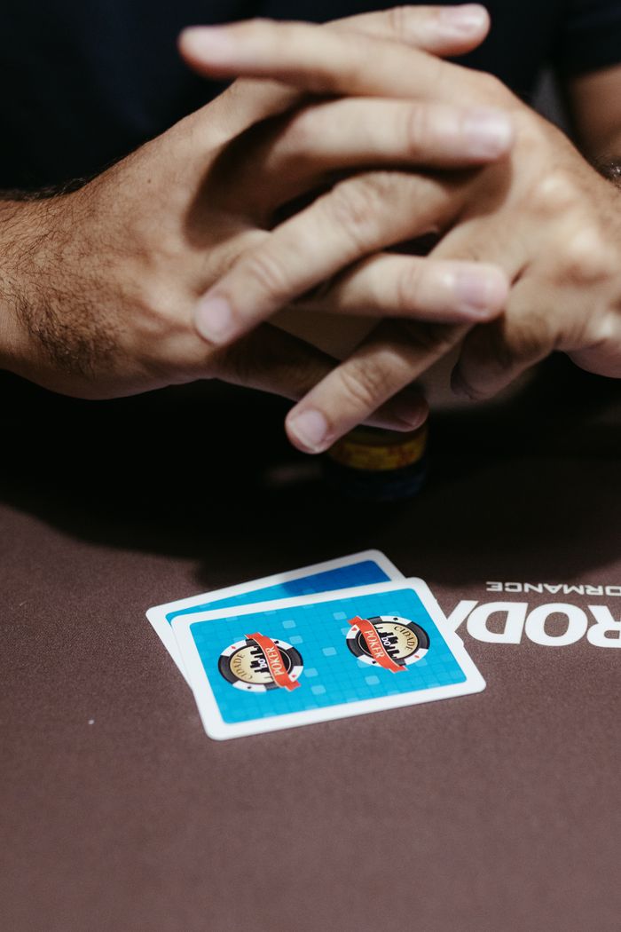 A poker player clasps hands over two face-down cards at a poker table, ready for the next move.