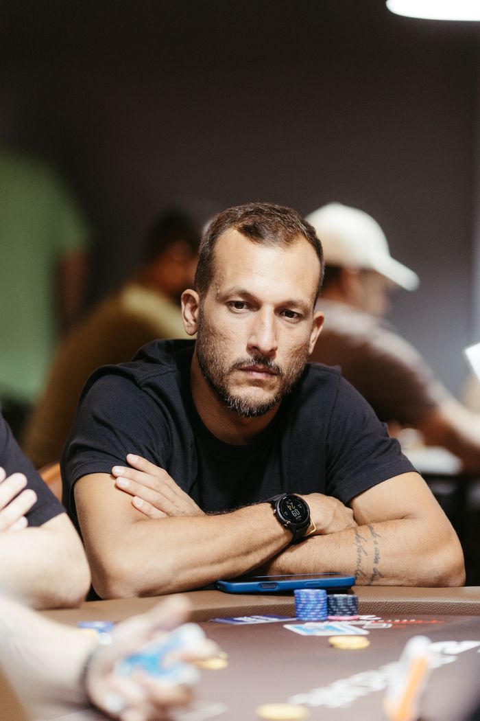 A focused poker player in a black shirt sitting at a table with poker chips indoors.