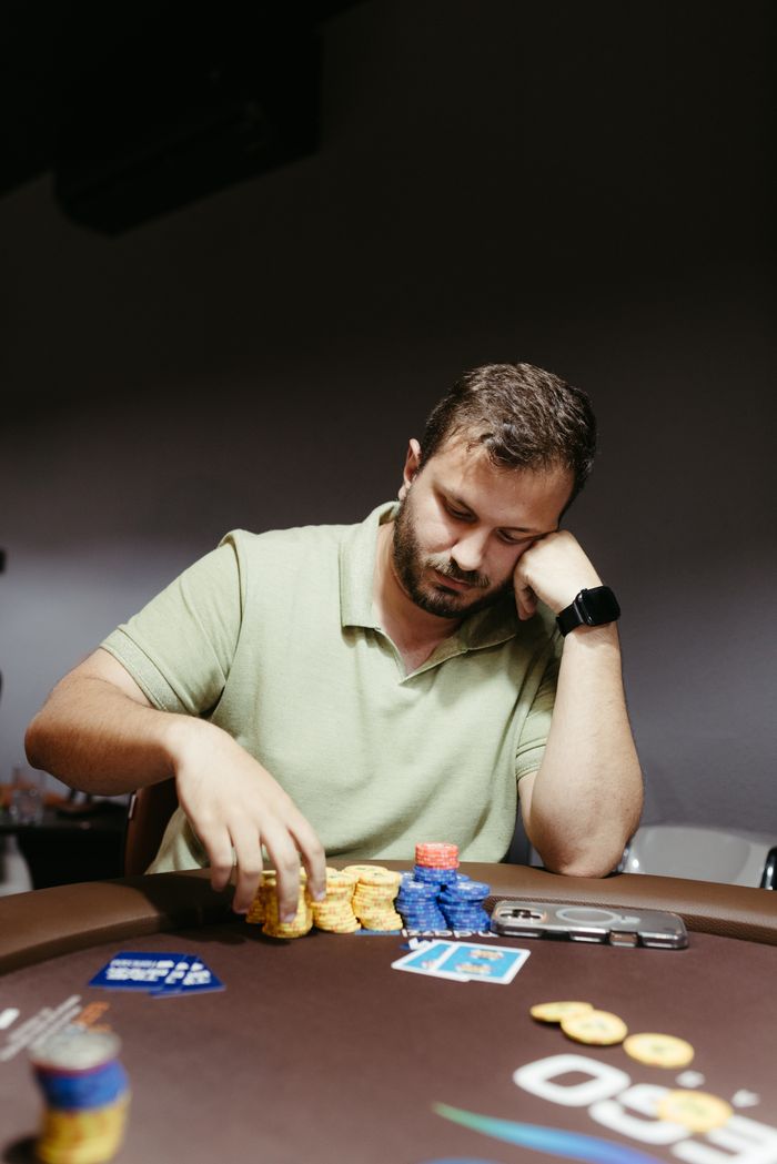 A thoughtful man plays poker indoors with colorful chips and cards on table.